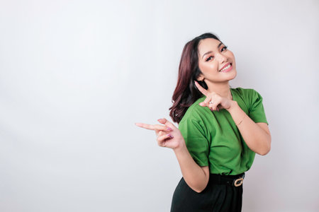Smiling beautiful Asian woman pointing finger sideward to empty space isolated white backgroundの写真素材