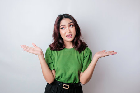 A portrait of an Asian woman wearing a green t-shirt looks so confused, isolated by a white...