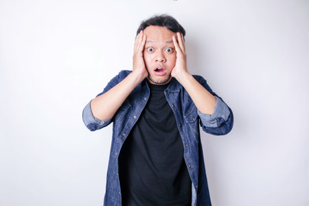 A portrait of a shocked Asian man wearing a navy blue shirt, isolated by a white backgroundの写真素材
