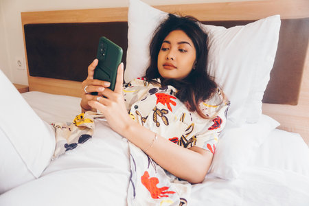 Serious concentrated young woman working from the bed. Hold the smartphone typing.の写真素材