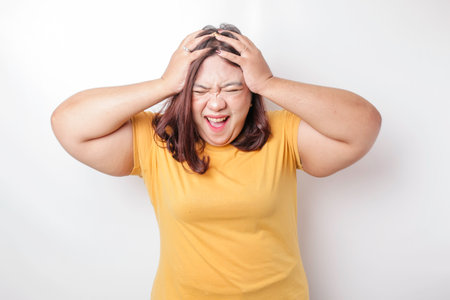 A portrait of an Asian big sized woman wearing a yellow t-shirt isolated by white background looks depressedの写真素材