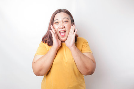 Young beautiful Asian big sized woman wearing a yellow shirt shouting and screaming loud with a hand on her mouth. communication concept.の写真素材