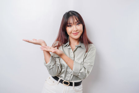 Excited Asian woman wearing sage green shirt pointing at the copy space beside her, isolated by white backgroundの写真素材