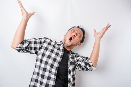 Shocked Asian man wearing tartan shirt pointing at the copy space on top of him, isolated by a white...