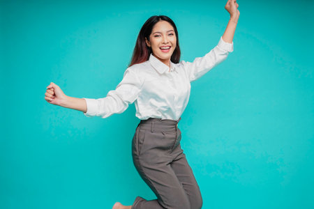 Photo of active Asian girl or employee jump raise hands up wear white shirt isolated blue color backgroundの写真素材