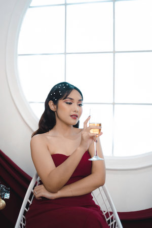 Portrait of pretty young girl cozy sit down and drinking wine, wear red gown in decorated Christmas living room indoorsの写真素材