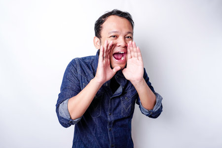 Young handsome man wearing a blue shirt shouting and screaming loud with a hand on his mouth....