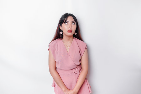 Dissatisfied young Asian woman dressed in pink blouse rolling her eyes and raising hand discontentedly, standing against white backgroundの写真素材