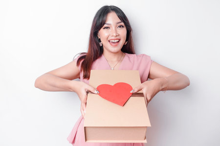 Beautiful young Asian woman dressed in pink blouse holding gift box red heart, Valentine's Day concept.の写真素材