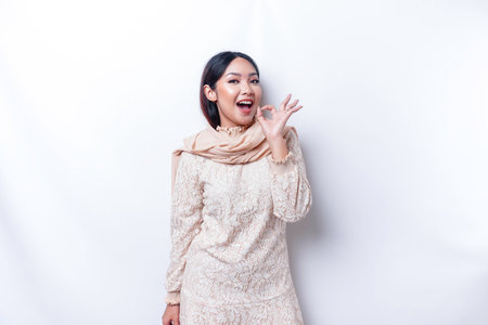 Portrait of a smiling Asian Muslim woman, giving an OK hand gesture isolated over white backgroundの写真素材