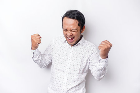 A young Asian man with a happy successful expression wearing white shirt isolated by white...