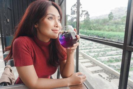 Portrait of joyful young woman enjoying a cup of tea at home. Smiling pretty girl drinking telang tea in rainy season.の写真素材