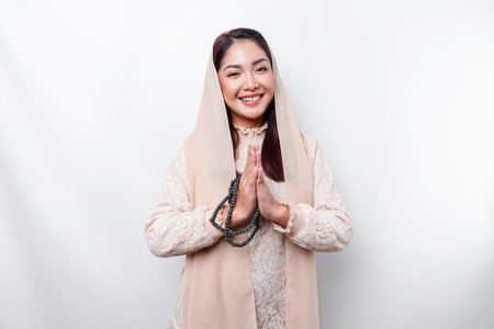 Portrait of a young beautiful Asian Muslim woman wearing a headscarf gesturing Eid Mubarak greetingの写真素材