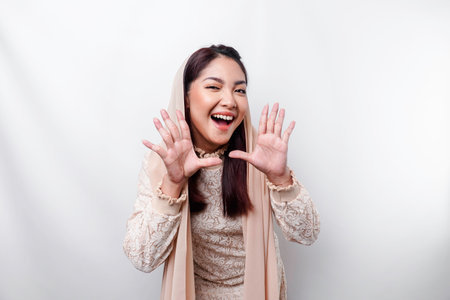 Young beautiful Asian Muslim woman wearing a headscarf shouting and screaming loud with a hand on her mouth. communication concept.の写真素材