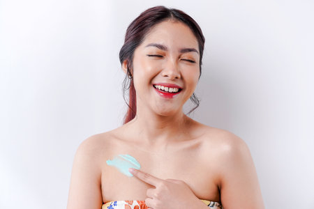 Skin Care Products Concept. Asian woman applying moisturizing lotion on body after shower, standing wrapped in towel, cropped imageの写真素材