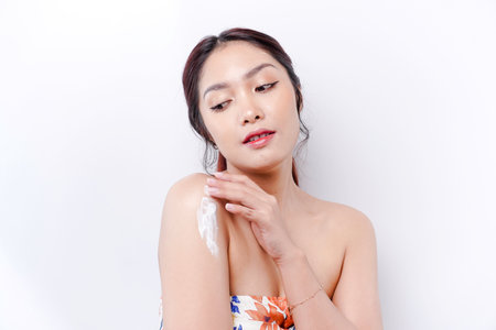 Skin Care Products Concept. Asian woman applying moisturizing lotion on body after shower, standing wrapped in towel, cropped imageの写真素材