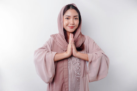 Portrait of a young beautiful Asian Muslim woman wearing a headscarf gesturing Eid Mubarak greetingの写真素材