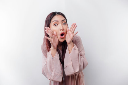 Young beautiful Asian Muslim woman wearing a headscarf shouting and screaming loud with a hand on her mouth. communication concept.の写真素材