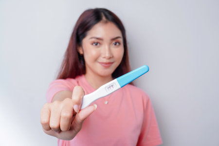 Happy young woman wearing pink t-shirt showing her pregnancy test, isolated on white background, pregnancy conceptの写真素材