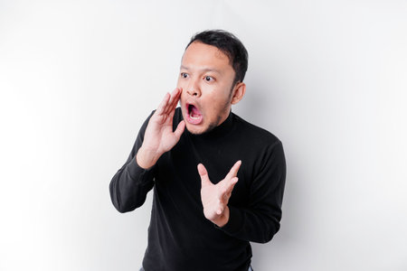 Young handsome man wearing a black shirt shouting and screaming loud with a hand on his mouth. communication concept.の写真素材