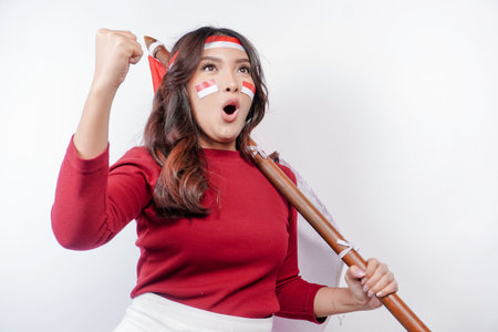 A young Asian woman with a happy successful expression wearing red top and headband while holding Indonesia's flag, isolated by white background. Indonesia's independence day concept.の写真素材