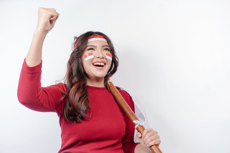 A young Asian woman with a happy successful expression wearing red top and headband while holding Indonesia's flag, isolated by white background. Indonesia's independence day concept.の写真素材
