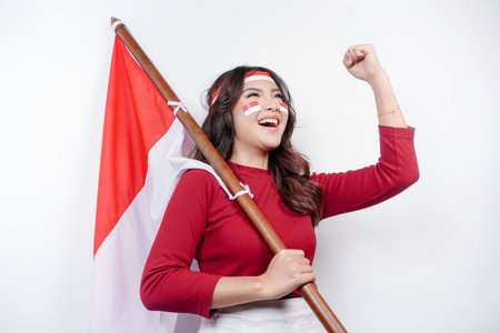 A young Asian woman with a happy successful expression wearing red top and headband while holding Indonesia's flag, isolated by white background. Indonesia's independence day concept.の写真素材