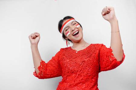 A young Asian woman with a happy successful expression wearing red kebaya and headband isolated by white background. Indonesia's independence day concept.の写真素材