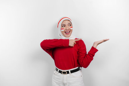 A happy Asian muslim woman wearing red top and white hijab, and pointing copy space beside her, isolated by white background. Indonesia's independence dayの写真素材