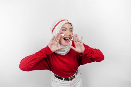 Young beautiful muslim woman wearing a red top and white hijab is shouting and screaming loud with a hand on her mouth. Indonesia's independence day concept.の写真素材