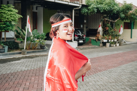 Happy smiling Indonesian woman wearing red kebaya holding Indonesia's flag to celebrate Indonesia Independence Day. Outdoor photoshoot conceptの写真素材