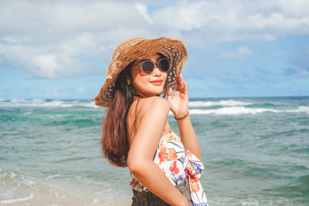 A happy young Asian woman wearing beach hat is posing to the camera at the beach in Gunungkidul, Indonesiaの写真素材