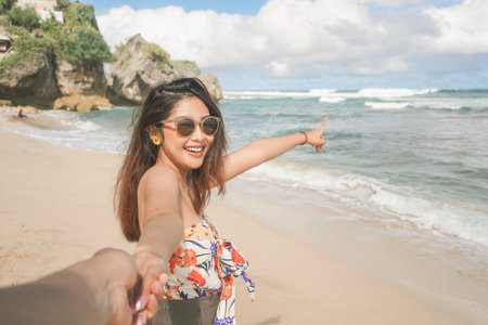 A happy young Asian woman is smiling to the camera and pointing at the beach in Gunungkidul, Indonesia.の写真素材
