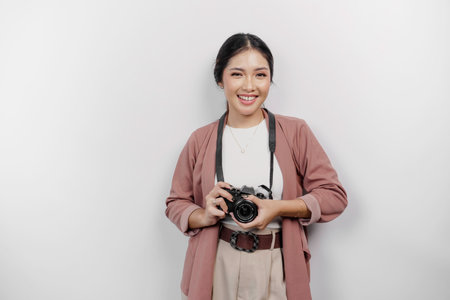 Cheerful young Asian woman tourist standing with camera taking photo isolated on white studio...