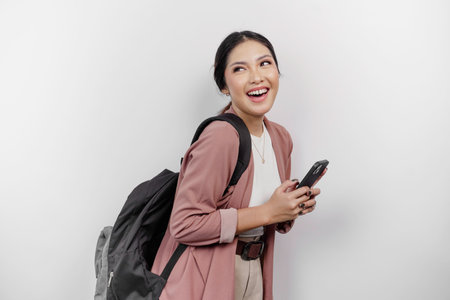 A thoughtful young Asian woman student wearing cardigan while holding a bag and handphone and looking aside to copy space, isolated by white background.の写真素材