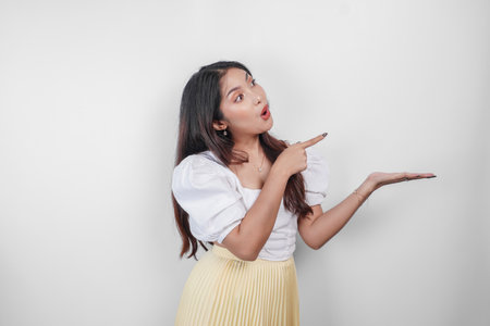 A shocked Asian woman with her mouth wide open and pointing copy space beside her, isolated by white background.の写真素材