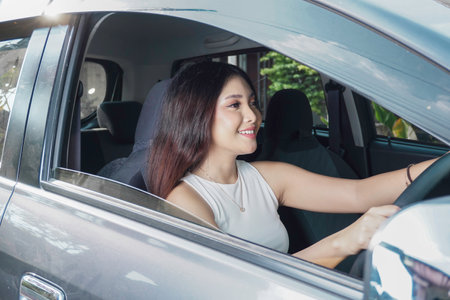 Attractive young Asian woman in casual wear is smiling while driving a car