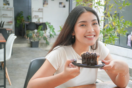 Young Asian woman holding and showing a black plate of doughnut pastry named cromboloni with chocolate filling for snack time, smiling with a happy and cheerful expressionの写真素材