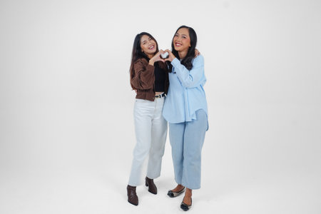 Two young Asian women expressing their tender feelings, shapes heart gesture expresses her love,...