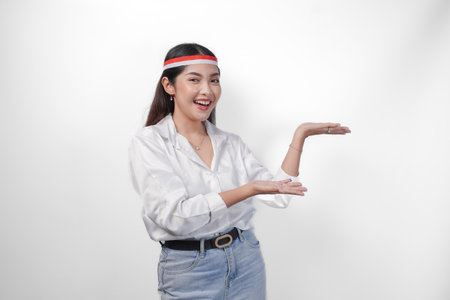 Excited Asian woman wearing flag headband presenting and pointing at the copy space on the side, smiling wide and standing on isolated white background. Independence day advertisement conceptの写真素材