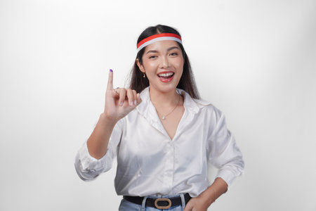 Young Asian woman proudly showing little finger dipped in purple ink after voting for president and parliament election, expressing excitement and happiness, wearing flag headband and white shirtの写真素材