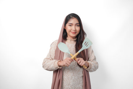 Beautiful Asian woman in veil hijab holding cooking utensils and making a refusal or rejection sign, saying no, asking to stop, standing over isolated white backgroundの写真素材