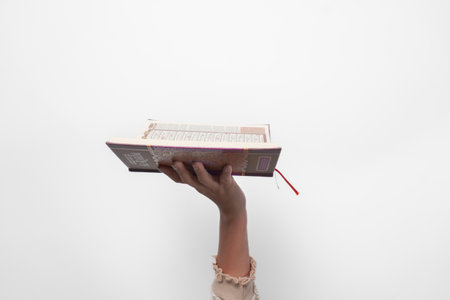 Close up portrait of Muslim woman hand lifting up Quran with open page, isolated by white background. Ramadan and Eid Mubarak conceptの写真素材
