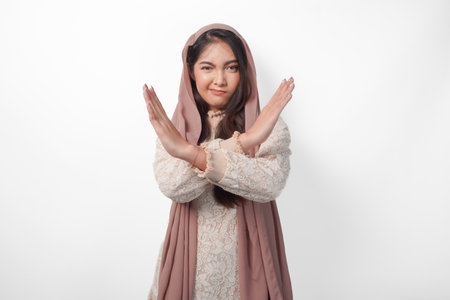 Young Asian Muslim woman wearing veil hijab gesturing a no rejection, refuse using hands and fingers, isolated by white background. Ramadan and Eid Mubarak conceptの写真素材