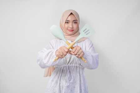 Displeased Asian woman in veil hijab doing a refusal or rejection sign, saying no, asking to stop gesture using spatula and cooking utensilsの写真素材