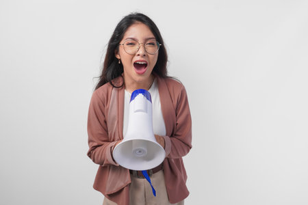 Young Asian woman wearing cardigan and eyeglasses shouting at megaphone, isolated on white background studio.の写真素材