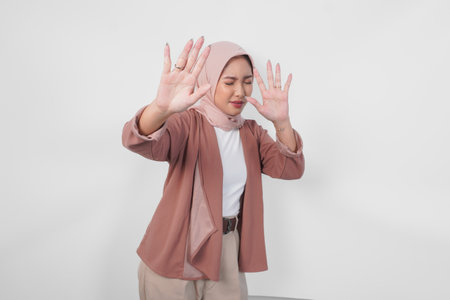 Beautiful Asian Muslim woman wearing a hijab with hand gesture posing rejection or prohibition, isolated by white background.の写真素材