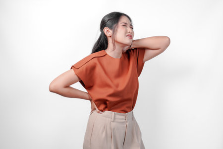 Tired young Asian woman in a brown shirt suffering from pain, muscle spasm on the neck isolated...