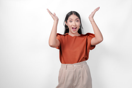 Excited young Asian woman in a brown shirt and taupe pants is presenting the copy space above her, isolated by white background.の写真素材