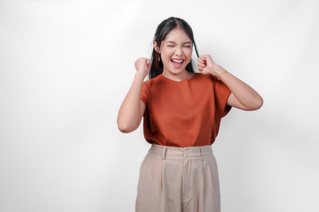 Joyful young Asian woman in a brown shirt with happy successful expression. Concept of happiness and excitement.の写真素材